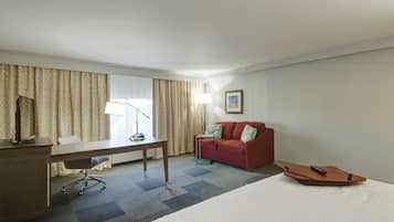 A hotel room with a desk, a red sofa, a bed, and a remote control on the bed.