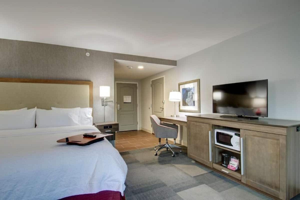 A hotel room with a bed, desk, TV, and microwave.