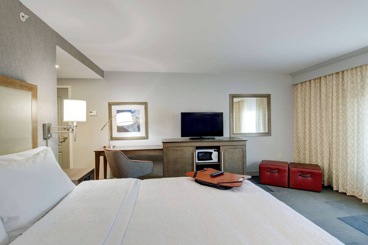 A hotel room with a bed, a desk with a television, a microwave, and two red suitcases.