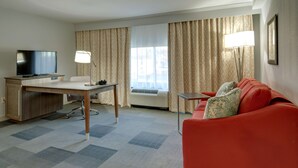 Habitación de hotel con escritorio, televisión, sofá rojo y ventanas amplias con cortinas.