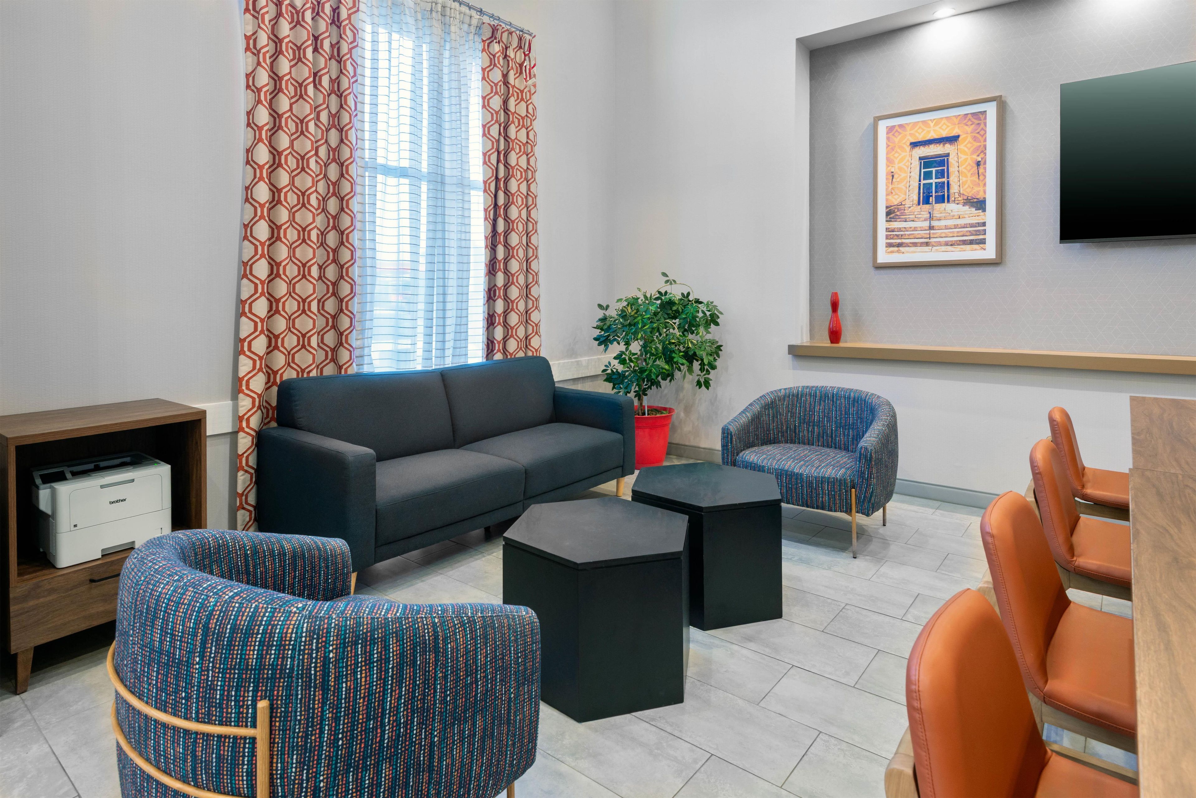 A modern living room with a sofa, two patterned armchairs, a coffee table, a potted plant, and a flat-screen TV mounted on the wall.