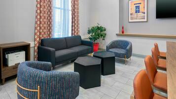 A modern living room with a sofa, two patterned armchairs, a coffee table, a potted plant, and a flat-screen TV mounted on the wall.