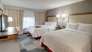 Una habitación de hotel con dos camas, un escritorio con computadora, televisor y lámpara.