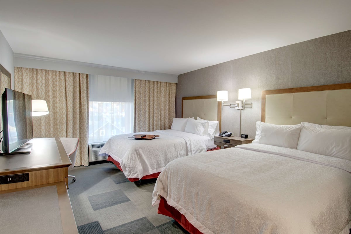 A hotel room with two beds, a desk with a computer, a TV, and a lamp.