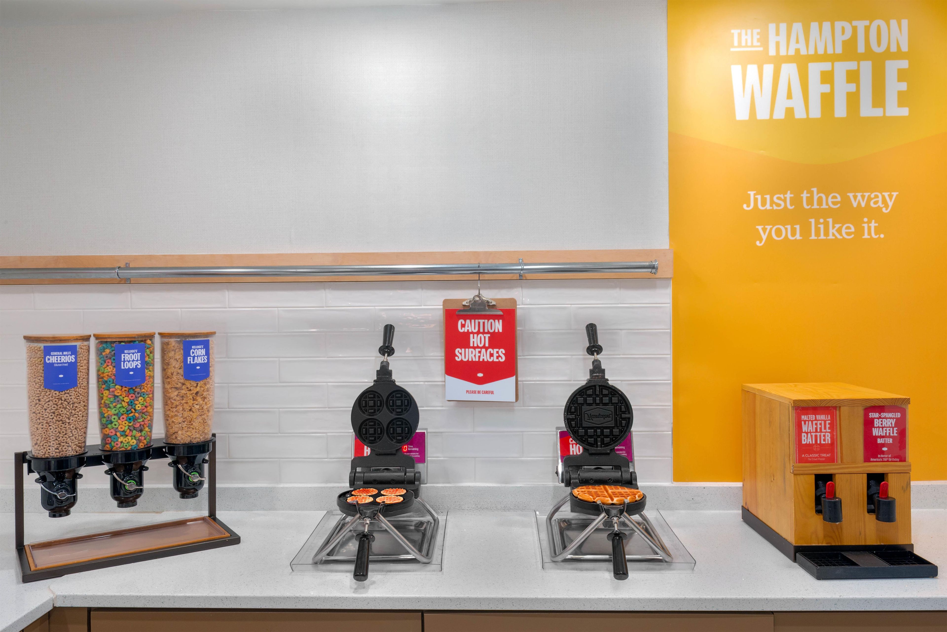 A kitchen counter with waffle makers, cereal dispensers, and waffle batter dispensers.