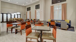 Un comedor amplio con varias mesas y sillas, un sofá y cortinas estampadas.