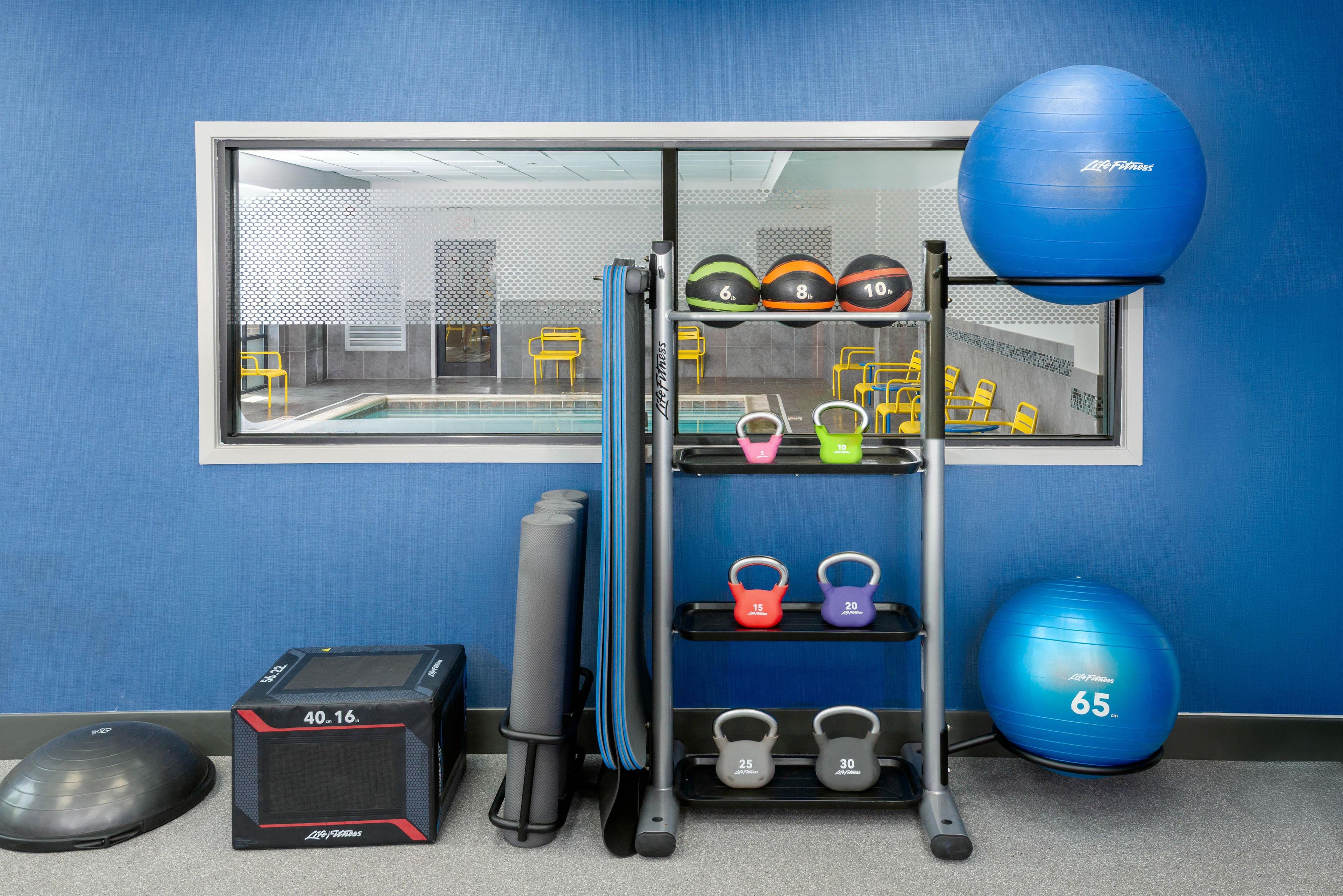 A gym with exercise equipment including a blue medicine ball, kettlebells, and a wall-mounted rack with various weights.