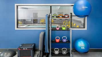 A gym with exercise equipment including a blue medicine ball, kettlebells, and a wall-mounted rack with various weights.