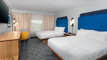 A hotel room with two beds, a desk, a chair, a TV, and a window with curtains.