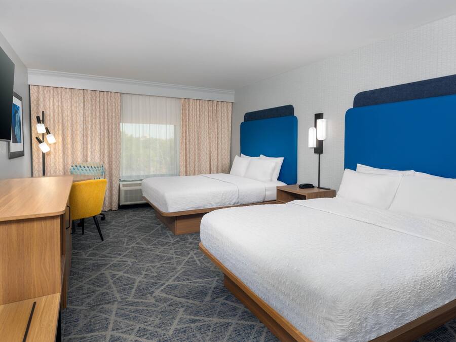 A hotel room with two beds, a desk, a chair, a TV, and a window with curtains.