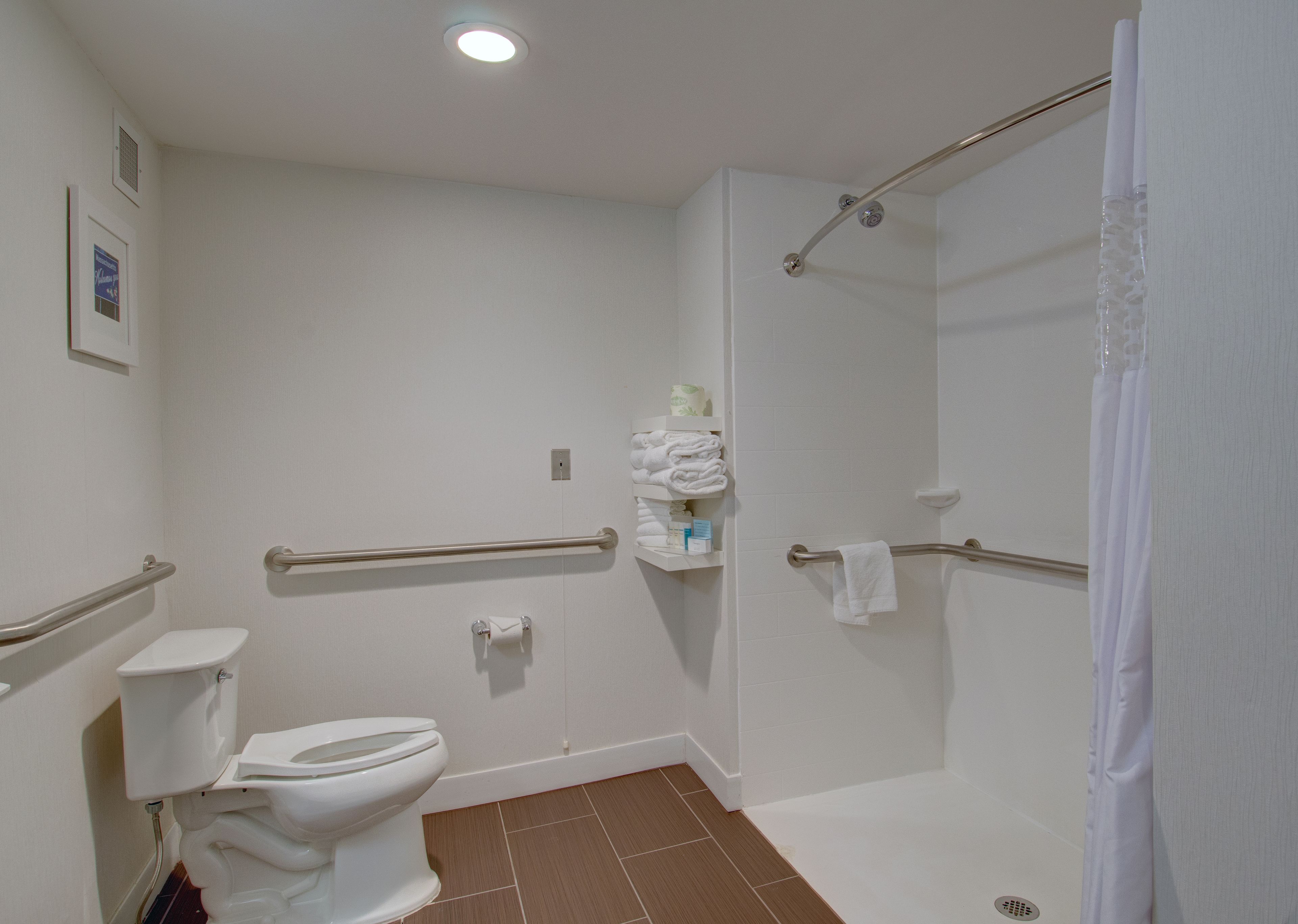 A bathroom with a toilet, a shower with a grab bar, and a towel rack.