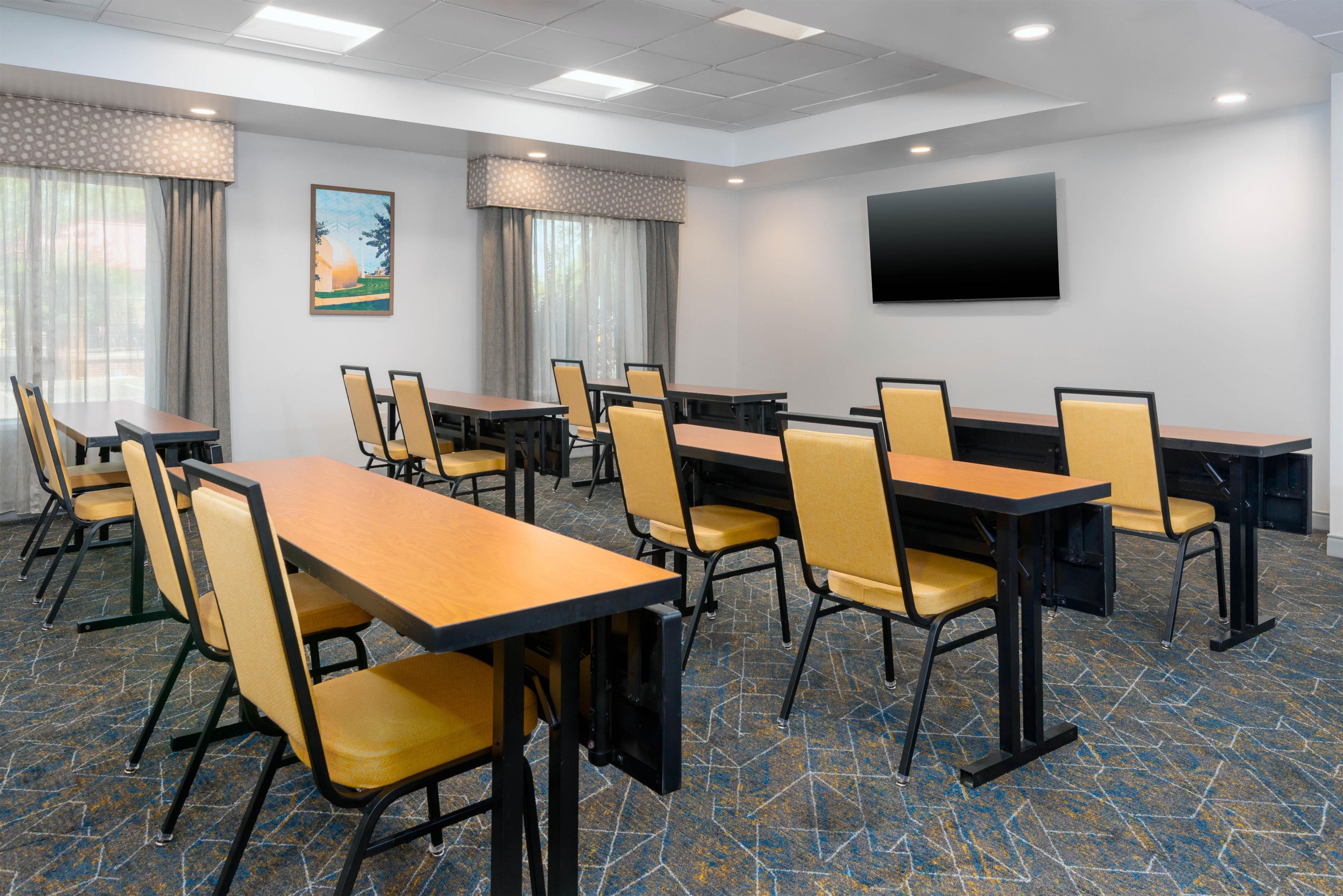 A conference room with tables and chairs, a flat-screen TV, and a painting on the wall.