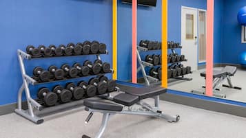 Un gimnasio con equipo de levantamiento de pesas, una banca y un espejo que refleja el equipo.