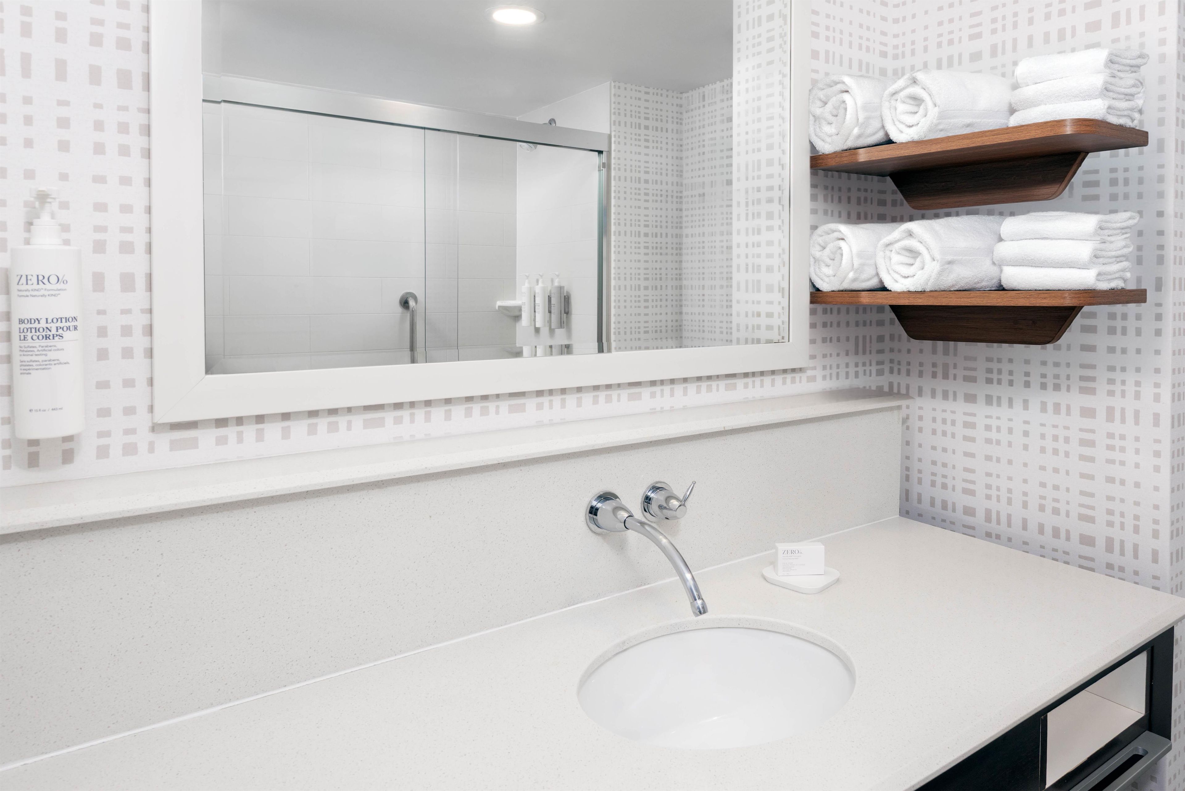 A modern bathroom with a large mirror, a sink, and wooden shelves holding rolled towels.