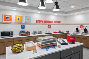 A breakfast buffet with labeled food stations, a microwave, and a kettle.