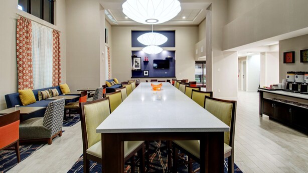 Un comedor de hotel con una larga mesa, sillas, un sofá y una lámpara colgante grande.