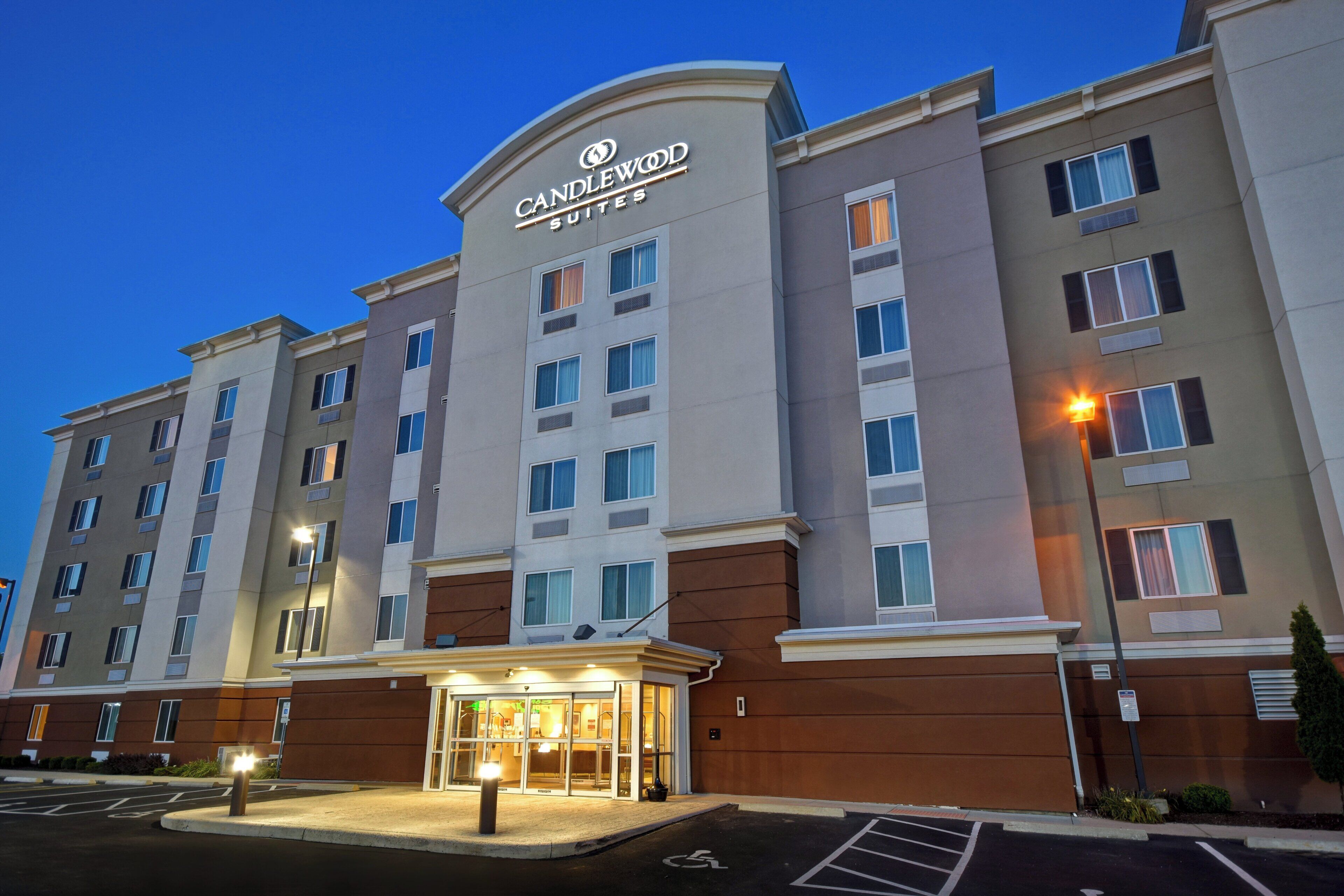 A multi-story hotel with a prominent 'CANDLEWOOD SUITES' sign, a parking lot, and a well-lit entrance.