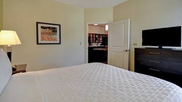 A hotel room with a bed, a television, a desk with a lamp, and a door leading to a bathroom.