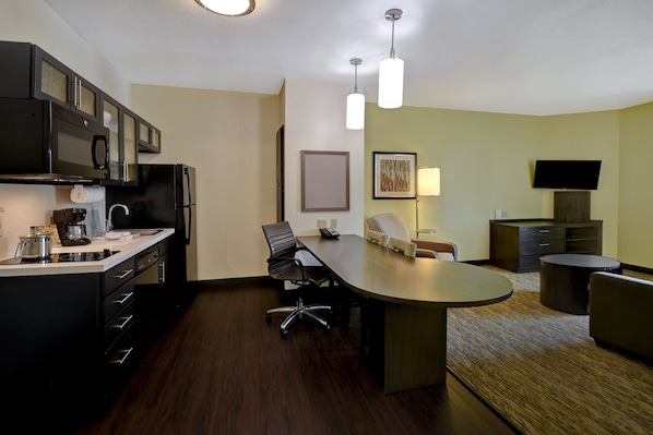 A modern hotel room with a kitchen area, a dining table, and a flat-screen TV. - Candlewood Suites St. Clairsville by IHG (St. Clairsville)