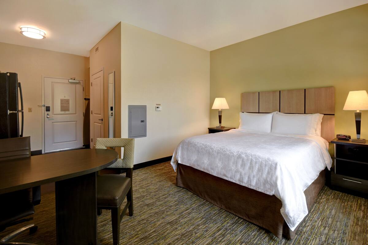 Une chambre d’hôtel équipée d’un lit, d’un bureau, d’une chaise, d’un réfrigérateur et d’une lampe.