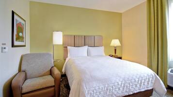 A hotel room with a bed, a chair, two bedside lamps, a framed picture on the wall, and a window with curtains.