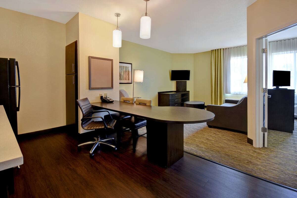 Une chambre d’hôtel moderne avec un plancher en bois, un grand bureau avec des chaises, un téléviseur à écran plat, un canapé et une table à manger.