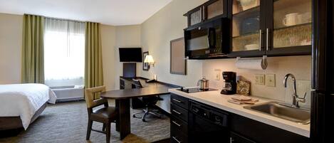 Habitación de hotel con cama, escritorio, silla, kitchenette y televisor.