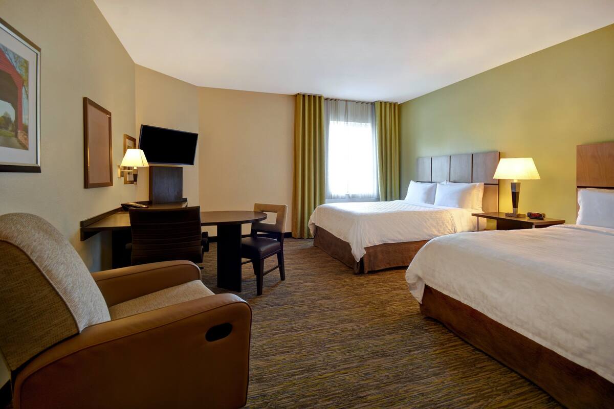 Une chambre d’hôtel avec deux lits, un bureau, une chaise, une télévision et une fenêtre avec des rideaux.