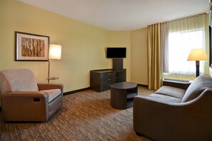 A hotel room with a sofa, armchair, flat-screen TV, and a small table. - Candlewood Suites St. Clairsville by IHG (St. Clairsville)