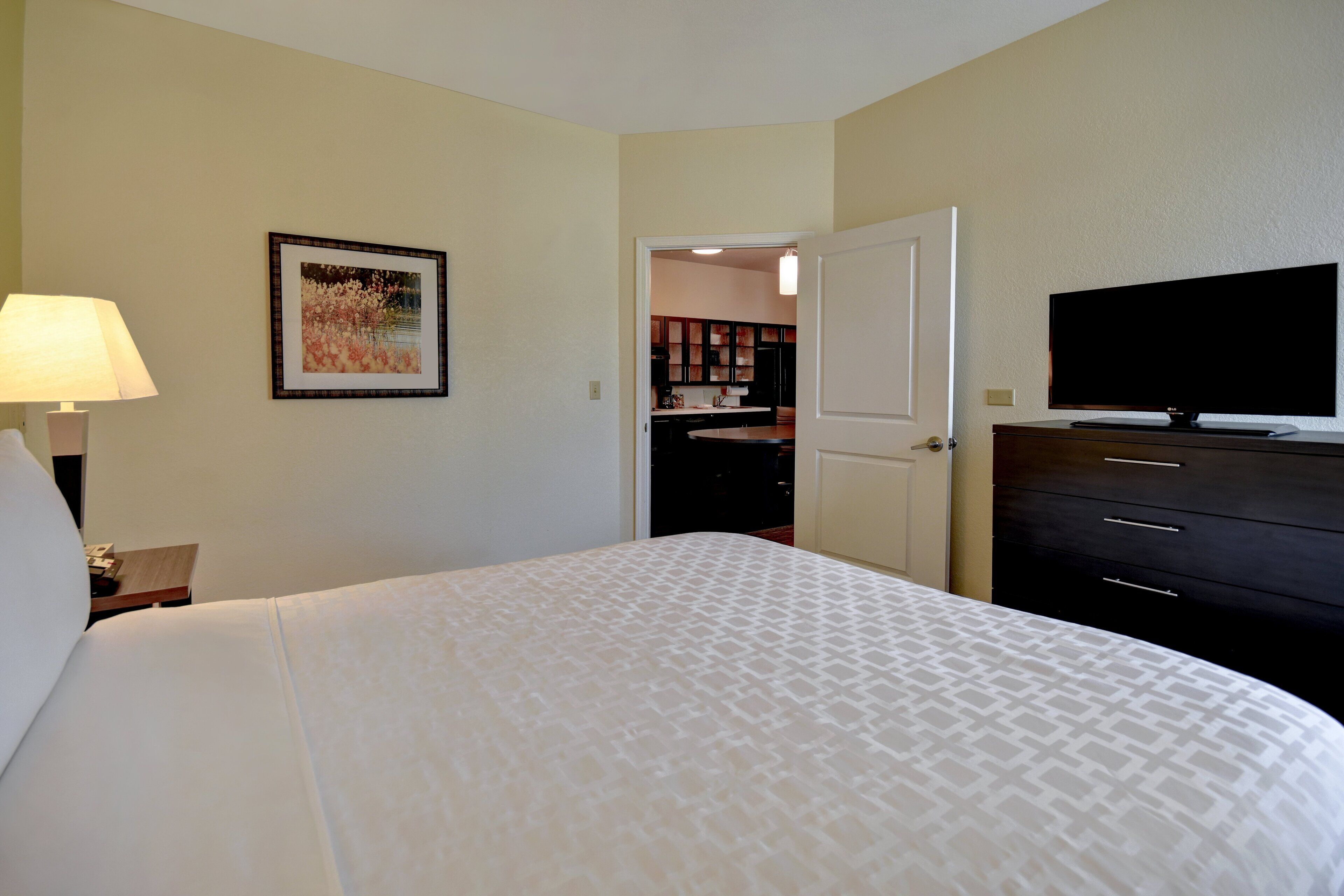 Habitación de hotel con cama, televisión, lámpara y un cuadro en la pared.