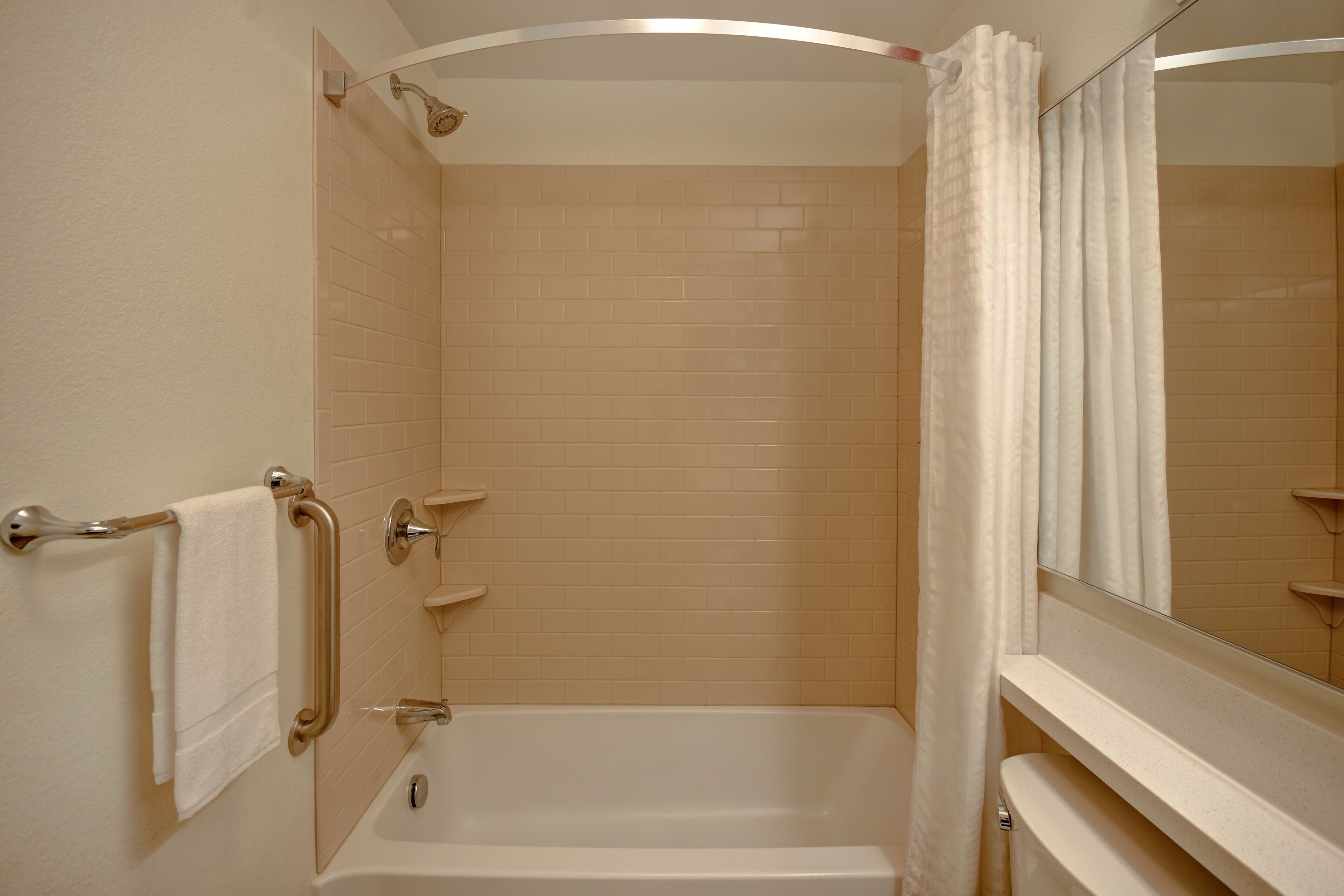 A bathroom with a bathtub, a handrail, a towel rack, and a mirror.