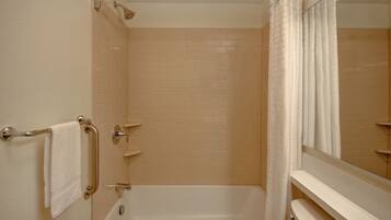 A bathroom with a bathtub, a handrail, a towel rack, and a mirror.