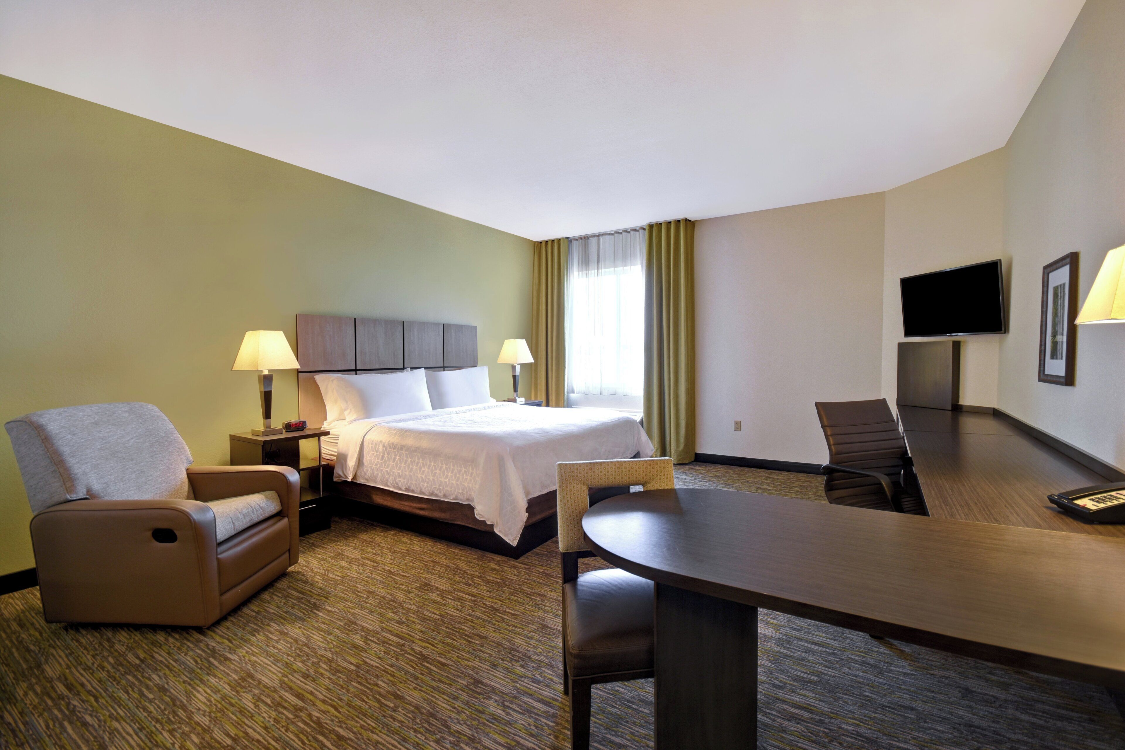 A hotel room with a bed, two bedside tables with lamps, a chair, a desk, and a television.