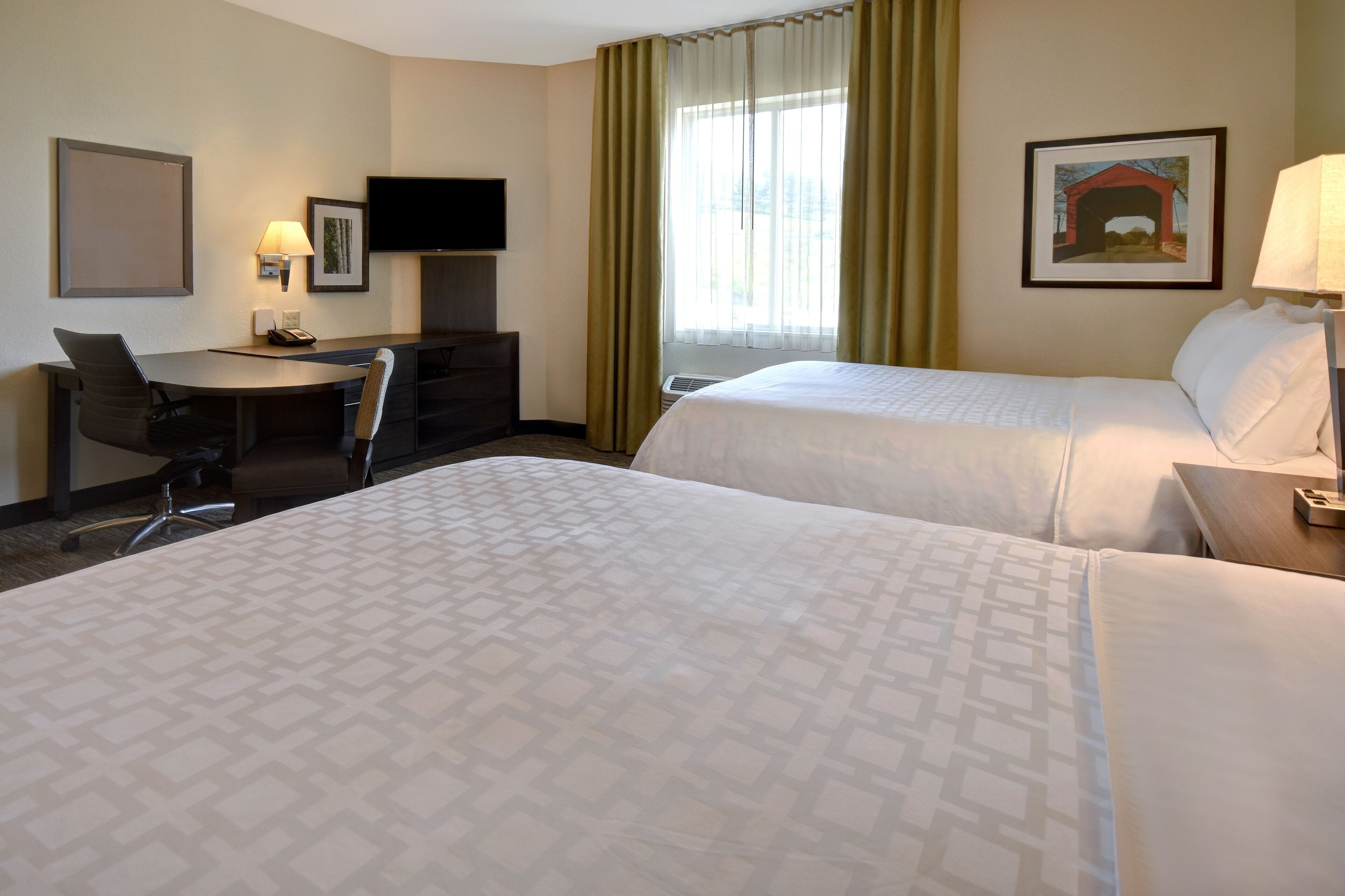 A hotel room with two beds, a desk with a chair, a television, and a painting on the wall.