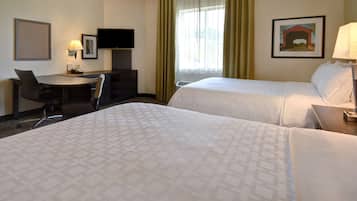 A hotel room with two beds, a desk with a chair, a television, and a painting on the wall.
