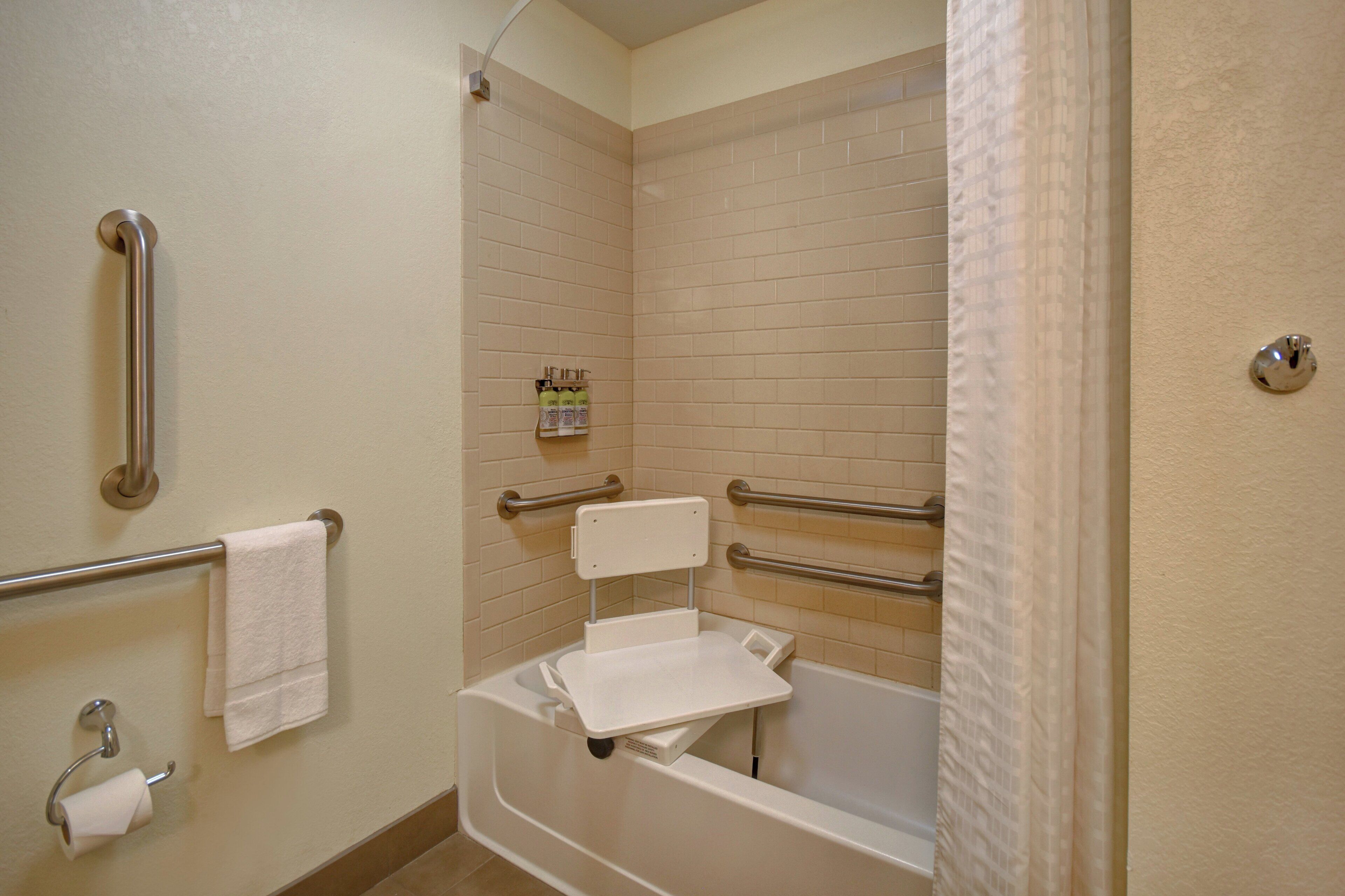 Une salle de bain équipée d’une baignoire, de barres d’appui, d’un porte-rouleau de papier toilette et d’un porte-serviettes.