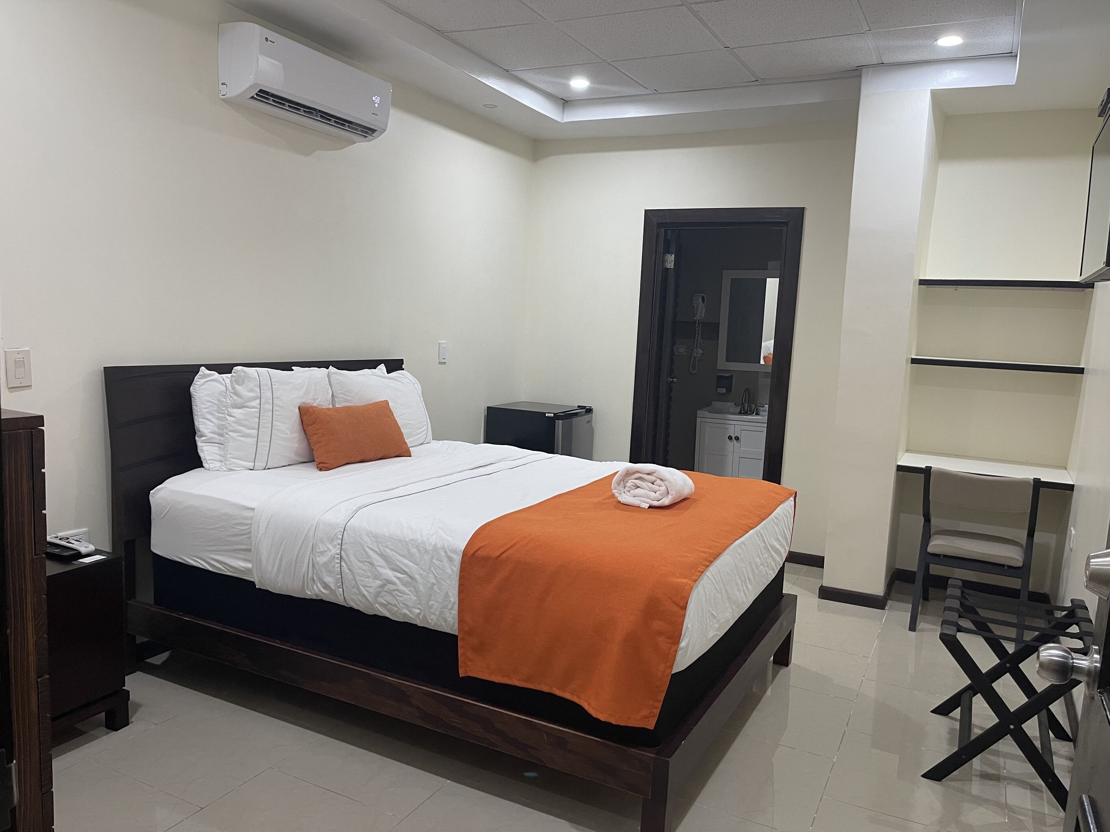 A neatly arranged hotel room with a bed, bedside table, and a small desk with a chair.