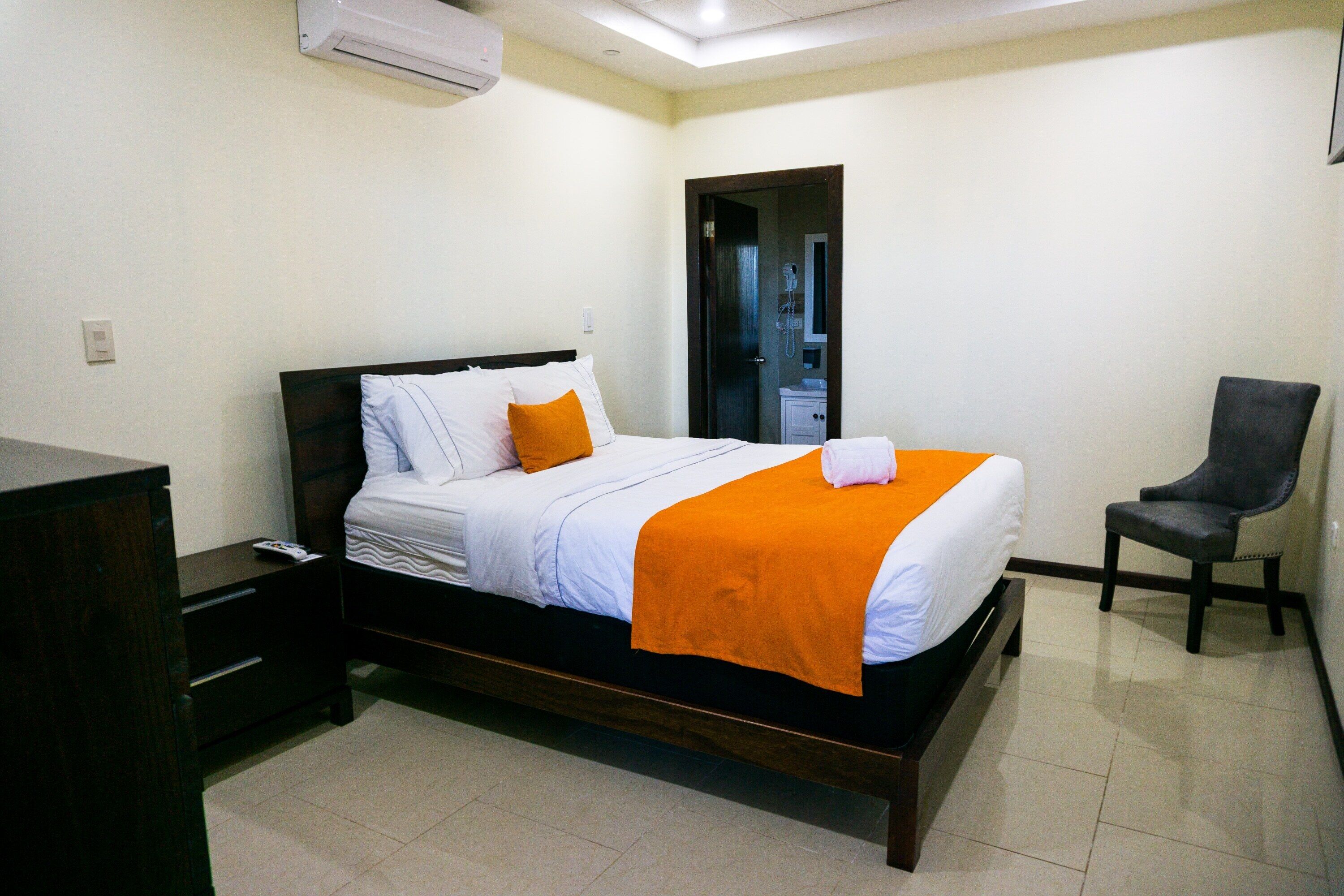A neatly made bed with an orange blanket, a wooden headboard, and a small bedside table with a phone.