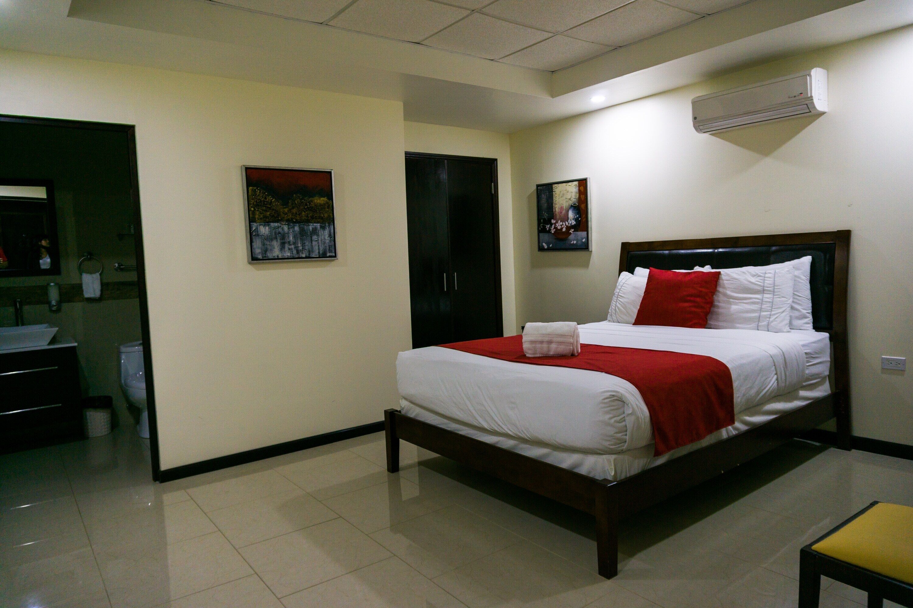 A neatly made bed with white and red bedding, a wooden headboard, and a small yellow chair.