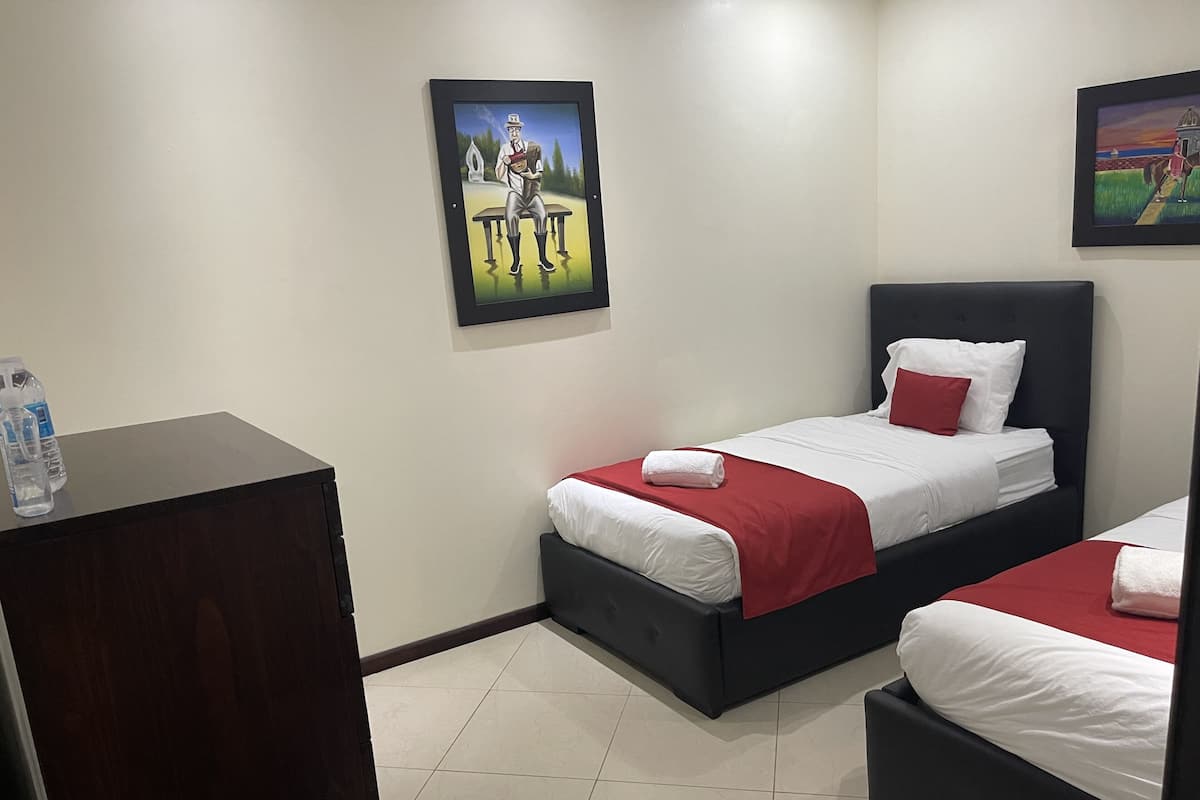 Ein Hotelzimmer mit zwei Betten, einem Holztisch und zwei gerahmten Kunstwerken an den Wänden.