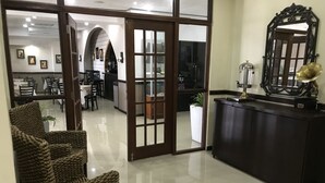 Un hall d’entrée avec un comptoir de réception, un grand miroir et un espace détente avec des fauteuils.