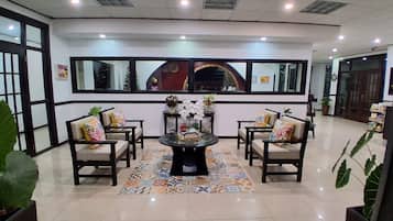 A lobby with a central round table, four chairs, a patterned rug, and a large mirror above the table.