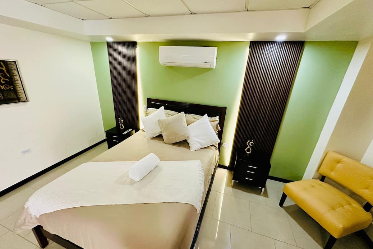 Ein modernes Hotelzimmer mit einem großen Bett, einem Nachttisch, einem Sessel und einer Klimaanlage.