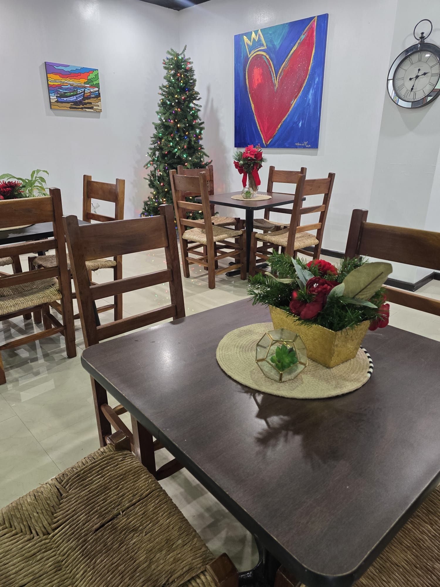 Un comedor con una mesa de madera, sillas, un árbol de Navidad y un cuadro en la pared.