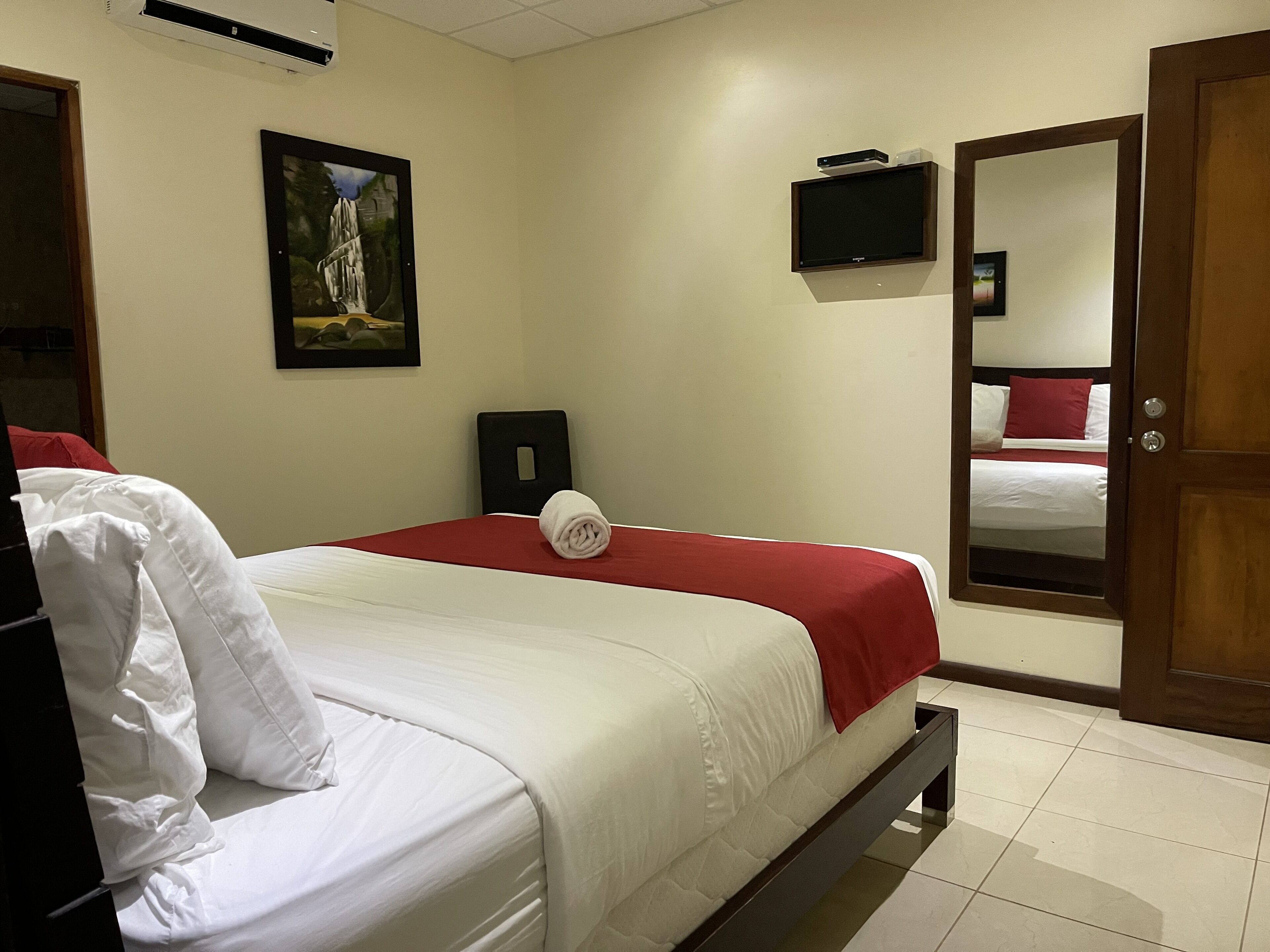 A hotel room with a bed, a TV, a painting, and a door.