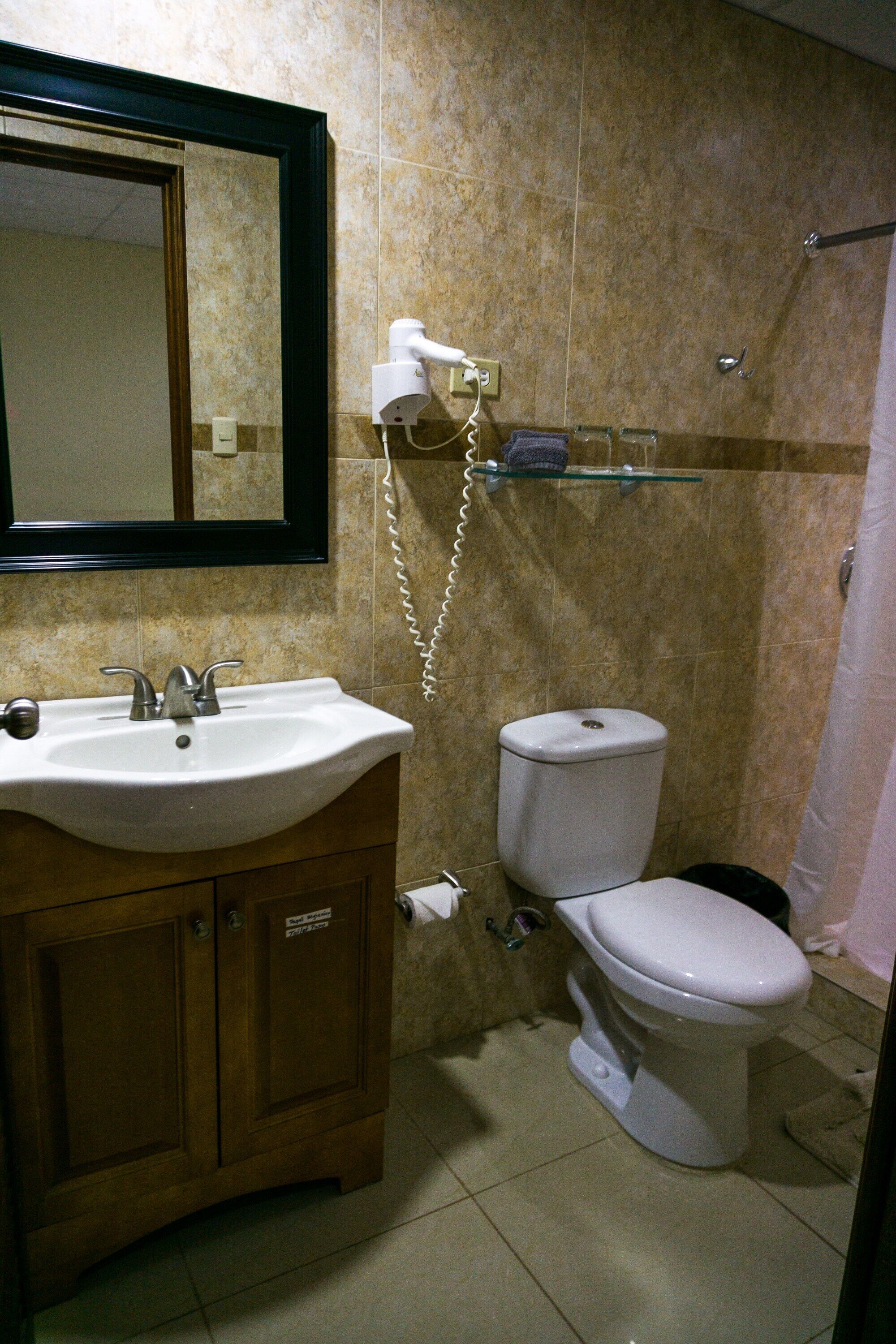 Ein Badezimmer mit Waschbecken, Spiegel, Toilette und Duschbereich.