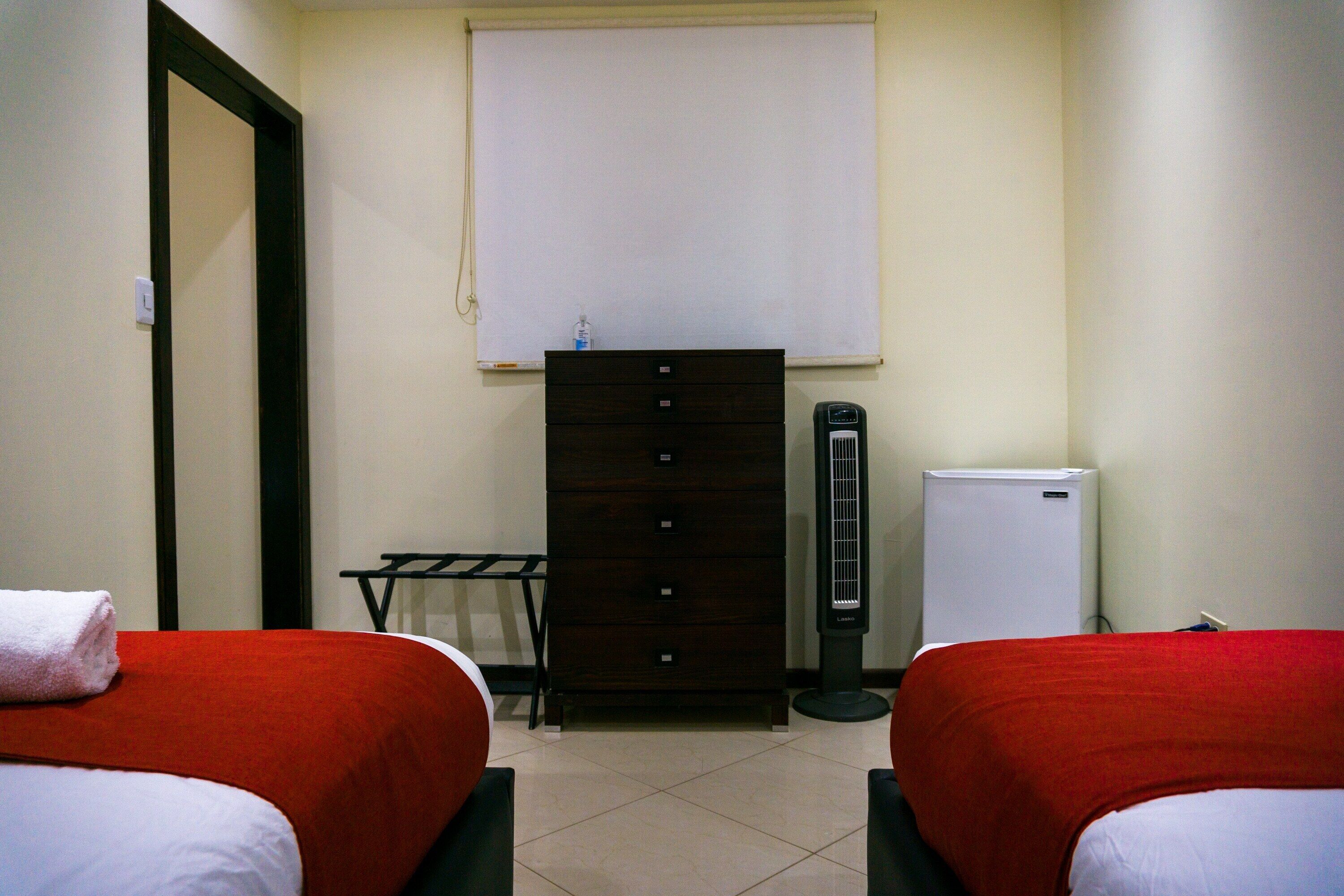 A hotel room with two beds, a dresser, a heater, and a window.