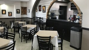 Un restaurant avec des tables et des chaises, un comptoir avec une machine à café et des tableaux encadrés aux murs.