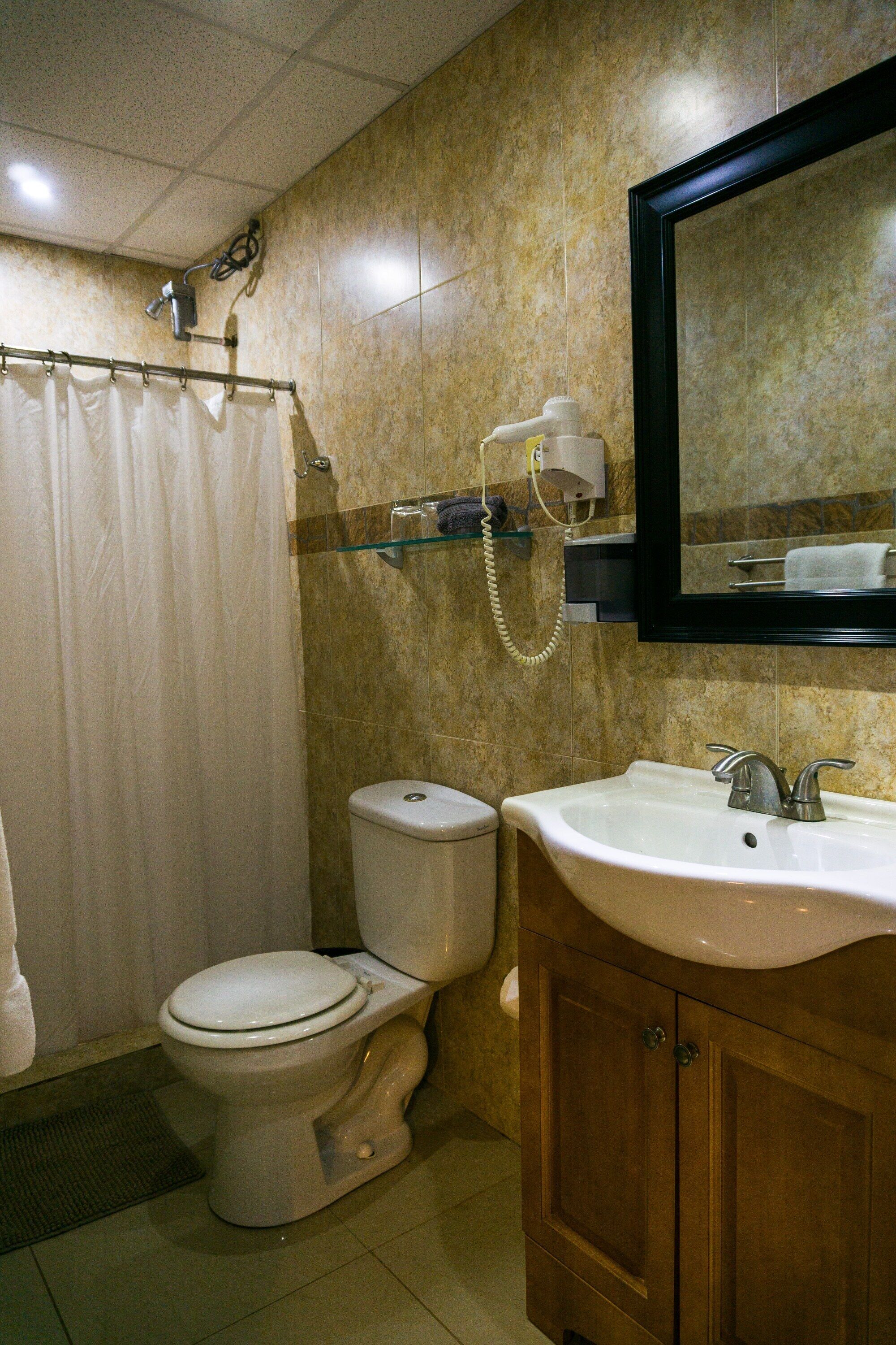 A bathroom with a toilet, sink, mirror, shower curtain, and a towel rack.
