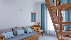 A modern living room with a sofa, wooden furniture, a small table with a vase, and a staircase. - Santellini Hotel (Santorini)